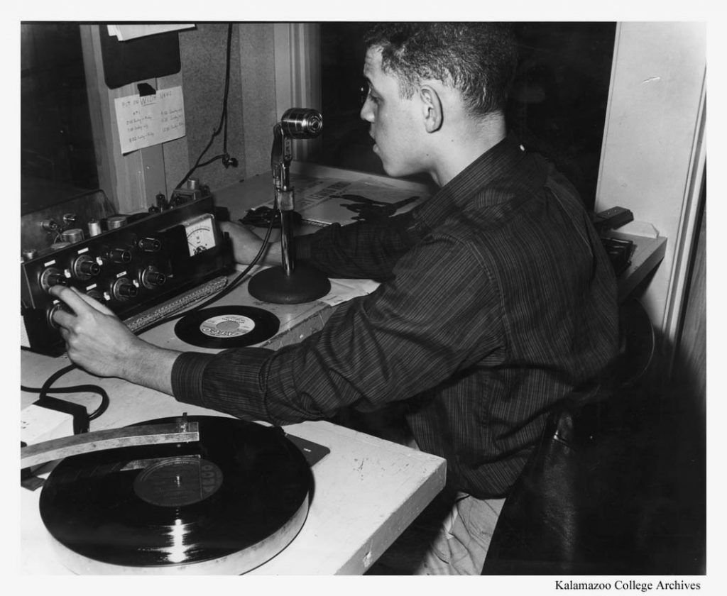 A student hosting a WJMD radio show sits in front of a microphone with a record player at his left.