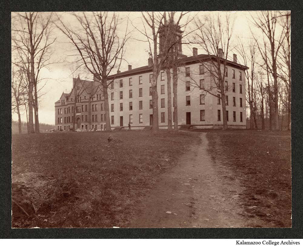 Path between bare trees leads to the 4 story limestone men's dormitory and Bowen Hall behind it.