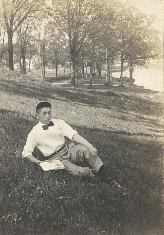 Japanese student Katsuji Kato sits on a grassy hill with an open book in one hand .